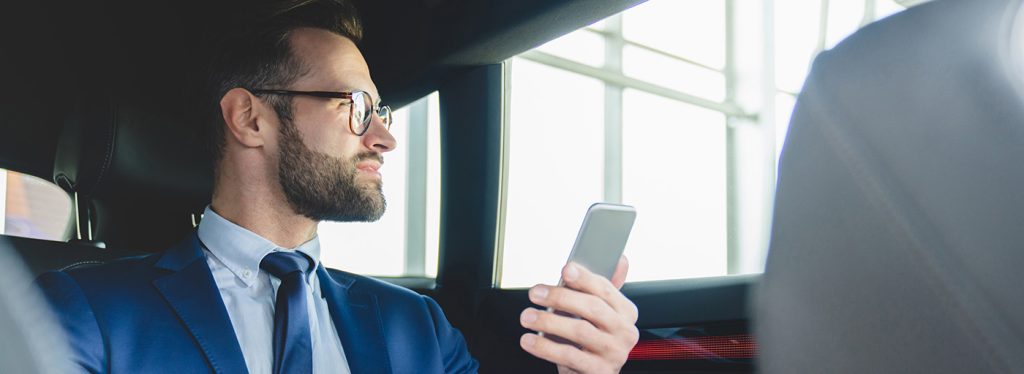 Arbeitszeiterfassung im Außendienst: Mitarbeiter sitzt im Auto mit einem Smartphone in der Hand