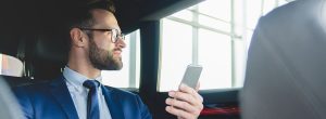Arbeitszeiterfassung im Außendienst: Mitarbeiter sitzt im Auto mit einem Smartphone in der Hand